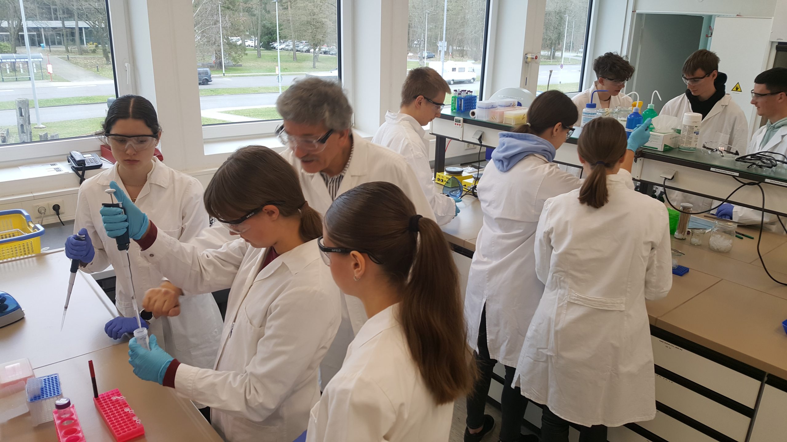 Auf diesem Bild sind Schülerinnen und Schüler in weißen Kitteln zu sehen, die im Labor arbeiten.