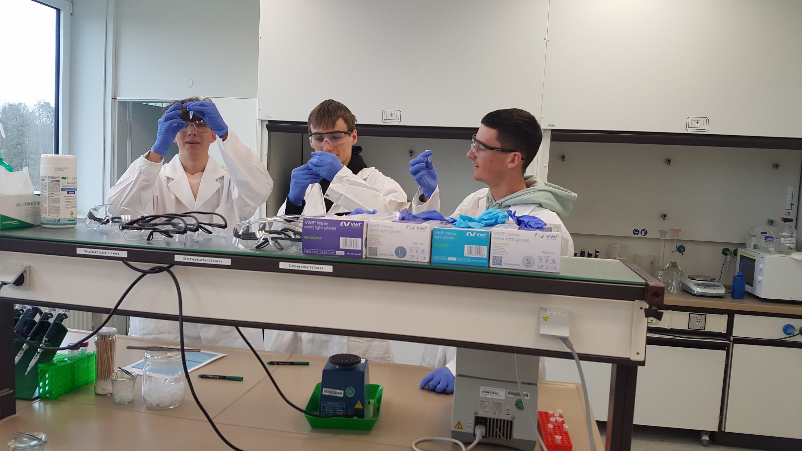 Auf diesem Bild sind Schülerinnen und Schüler in weißen Kitteln zu sehen, die im Labor arbeiten.